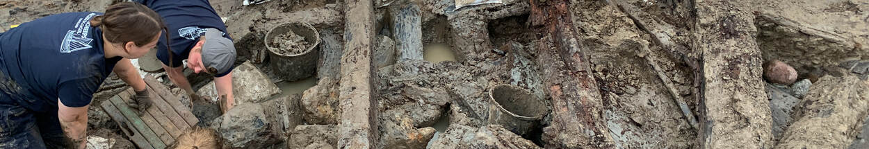 Foto van de opgraving van het Waterschip met archeologen in de modder, van boven gezien